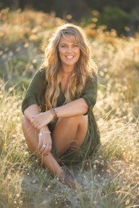 Photo of author Emma Mildon sitting in a field of grass and smiling at the camera